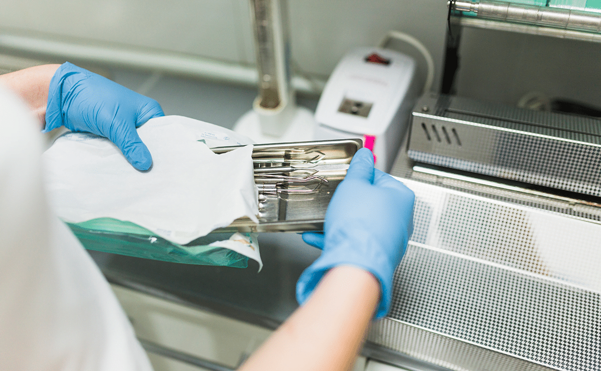 Photo of a nurse handling sanitised instruments near a stainless steel counter.